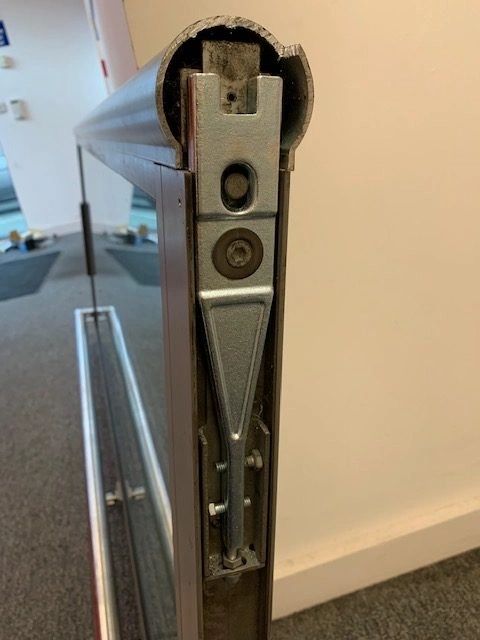 The top rail of a glass commercial door with the closer arm shoe and fixings exposed