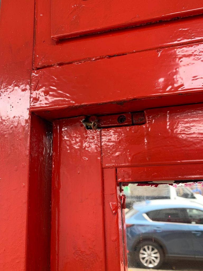 A weather-worn red timber shop front door with cracked gloss paint and a damaged hinge