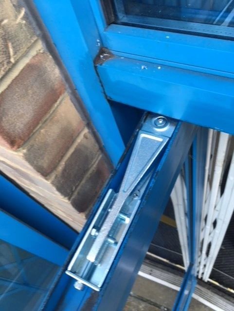 A door closer loading arm and bracket fitted to the head of a blue commercial door